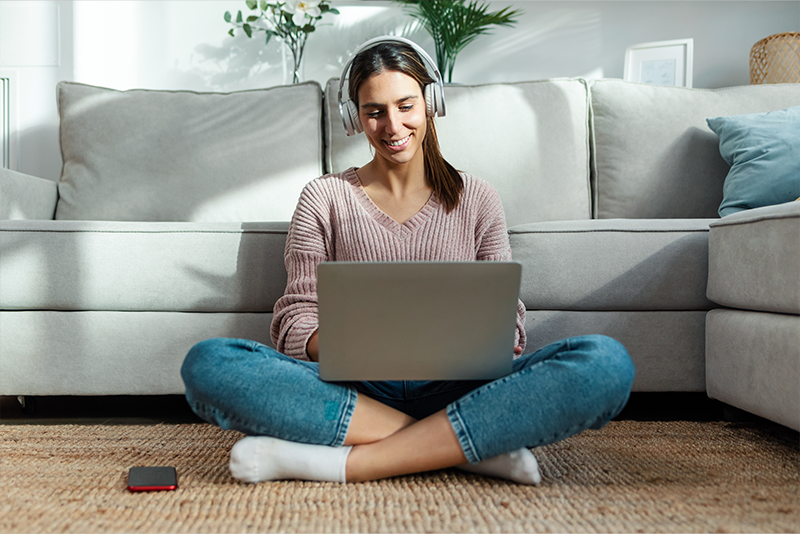 young-woman-listening-music-with-headphone-while-working-with-laptop-sitting-on-the-floor-at-home-800×534